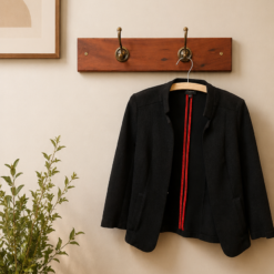Beige wall with a wooden coat rack holding a black blazer on a hanger, beside a framed botanical print and a potted plant.