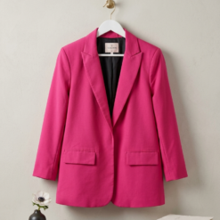 Bright pink blazer on a white hanger against a light wall, with a small vase and books nearby for decor.